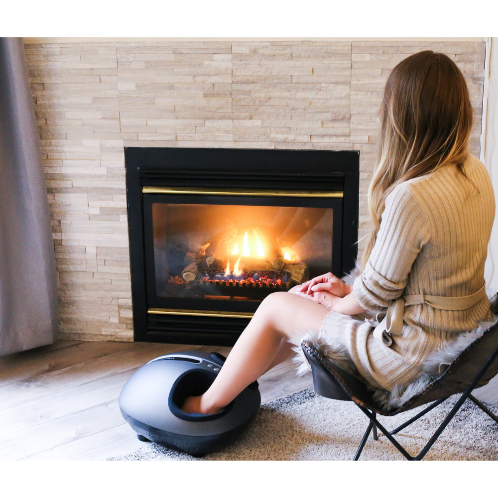 Woman using BACKplus® Shiatsu Foot Massager with Calf Compression in front of a fireplace