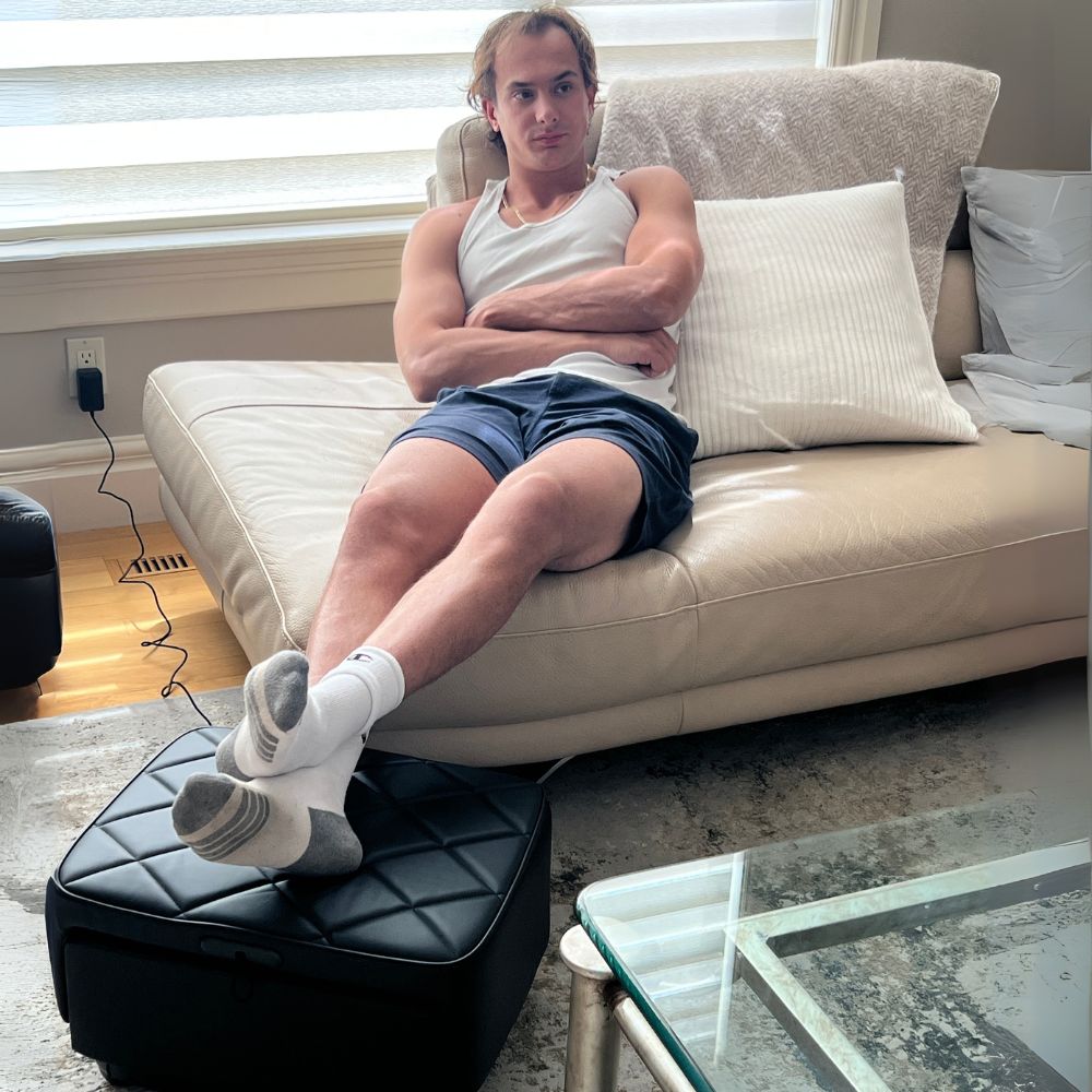 Man relaxing on couch using the BACKplus Ottoman Massager as an ottoman