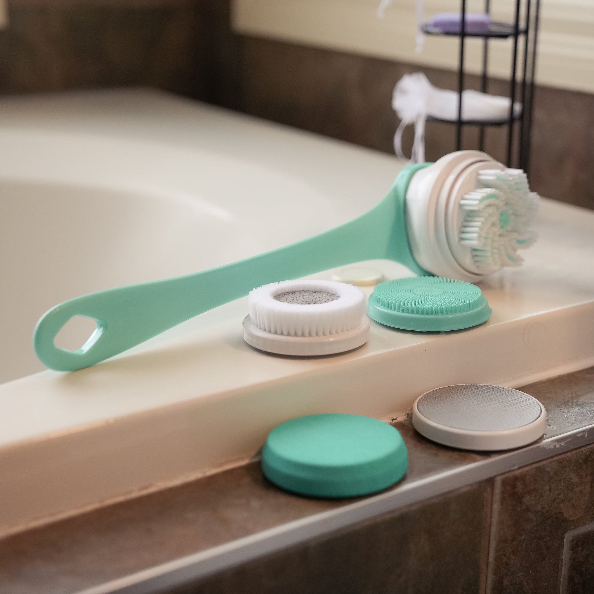 ShowerME Shower Brush in teal on the edge of a bathtub